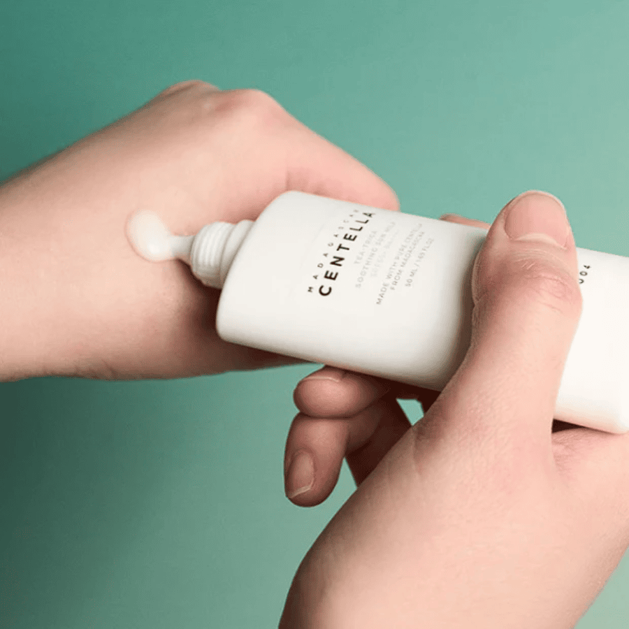 SKIN1004 - Tea-Trica Soothing Sun Milk 50 ml Hånd, der påfører ansigtspleje med Centella-ekspert serum fra My Skin, lyserød hud, grøn baggrund, skincare Produkt.